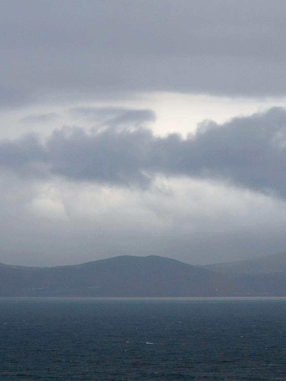 Overcast sky with dark clouds over a body of water and distant hills or mountains.
