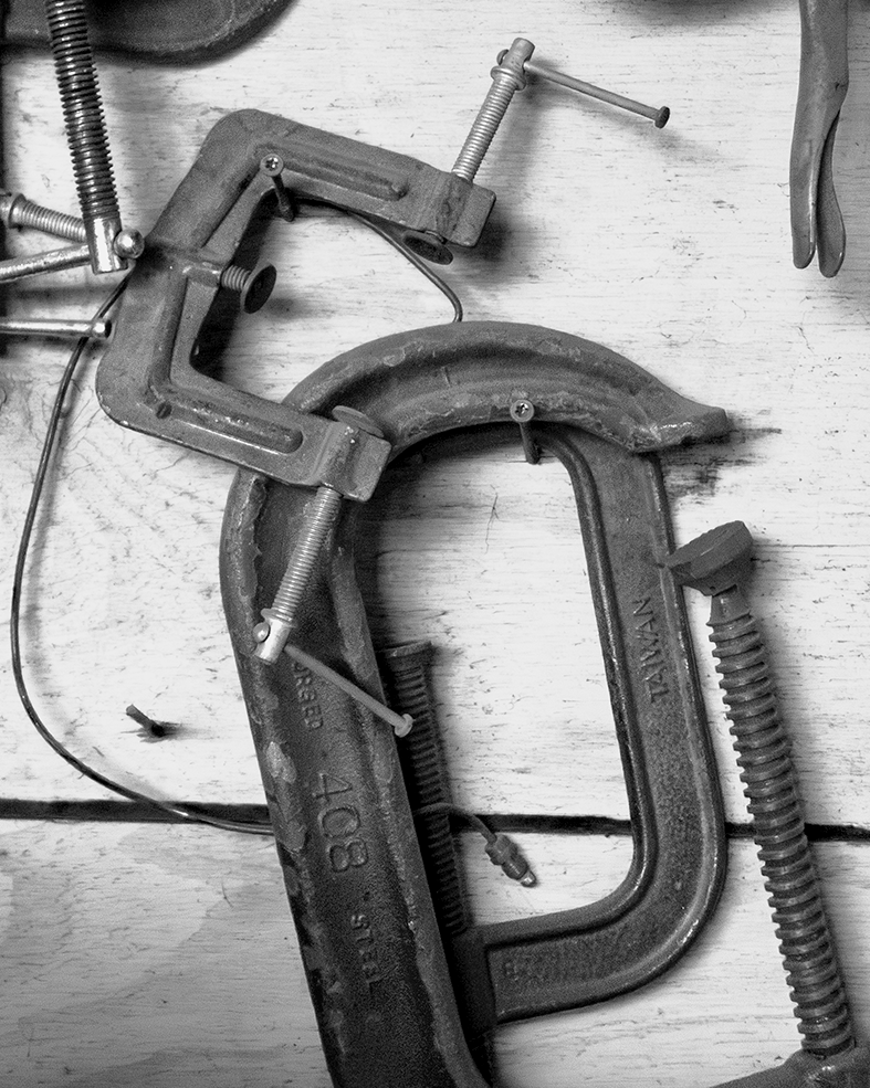 Close-up of multiple metal C-clamps and clamps on a wooden surface.