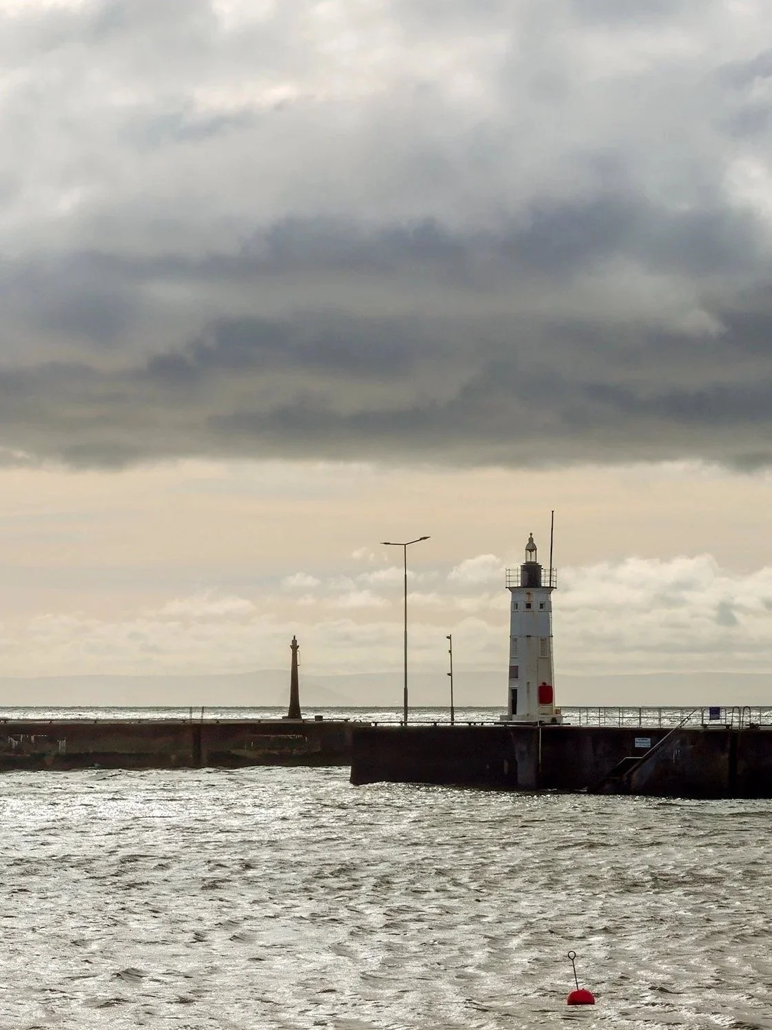 A lighthouse on a pier over water with a cloudy sky overhead.