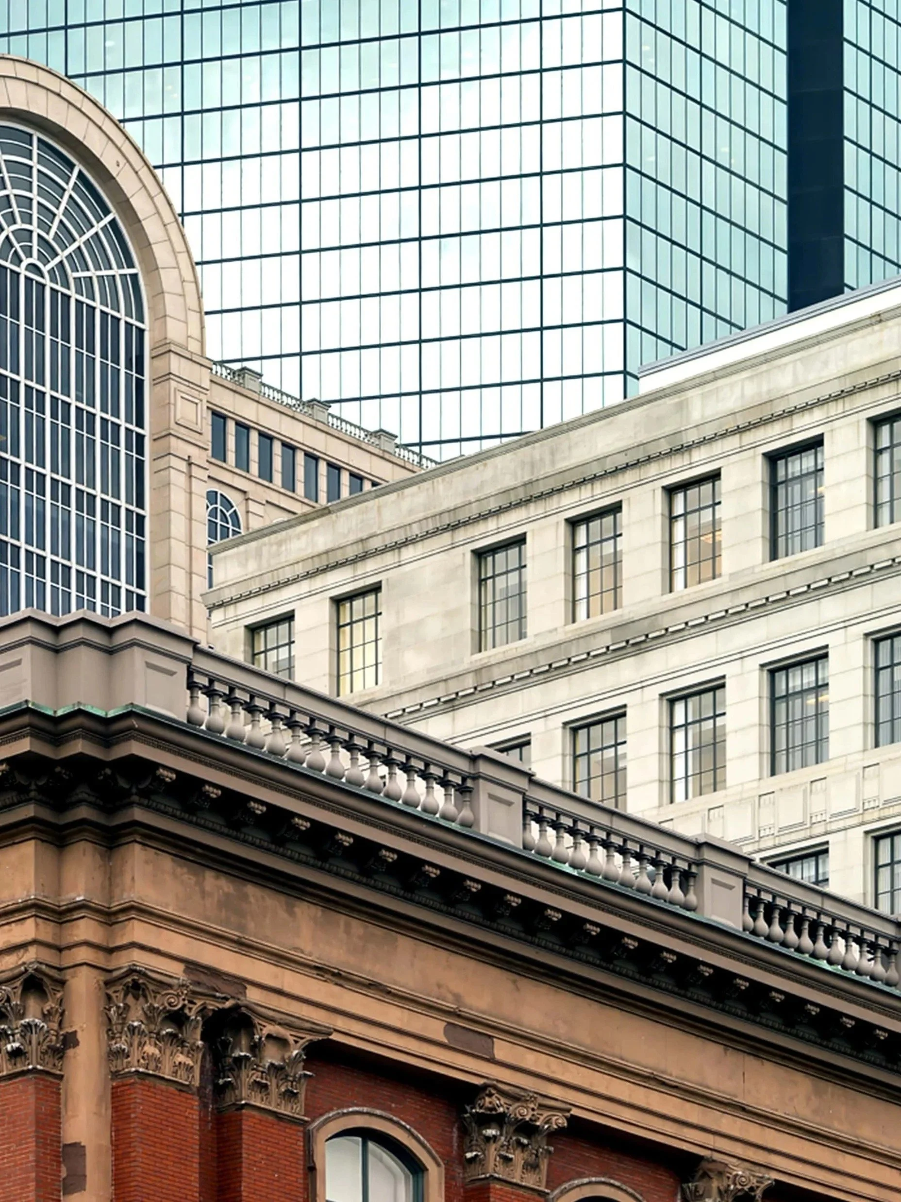 Multiple buildings with different architectural styles in an urban skyline, including a glass skyscraper, a historic stone building, and a brick structure with ornate details.