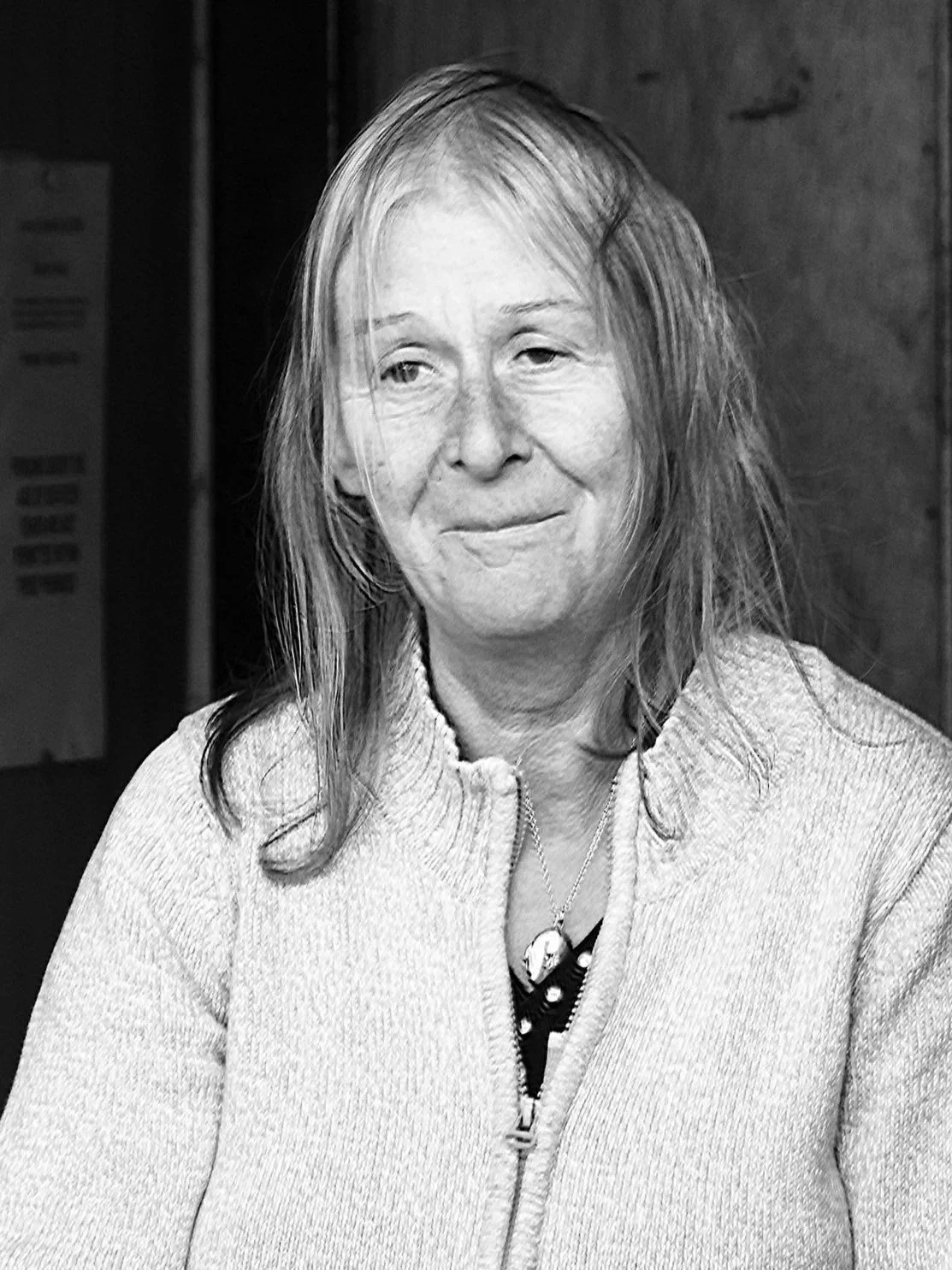 Black and white photo of a woman with long hair, wearing a zip-up sweater, with a slight smile, indoors.