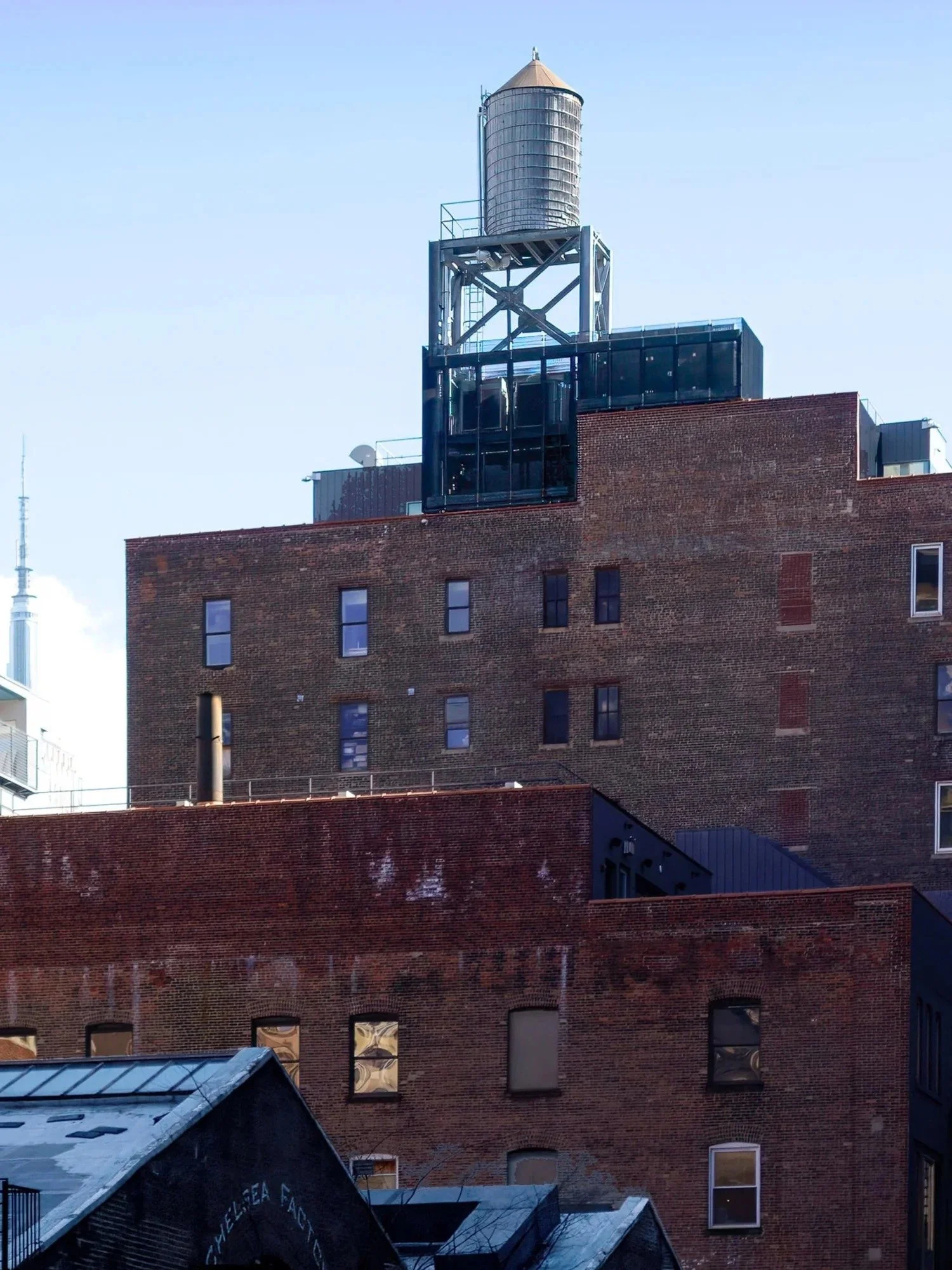 Close-up of a multi-story brick building with a water tower on the rooftop, against a clear blue sky.
