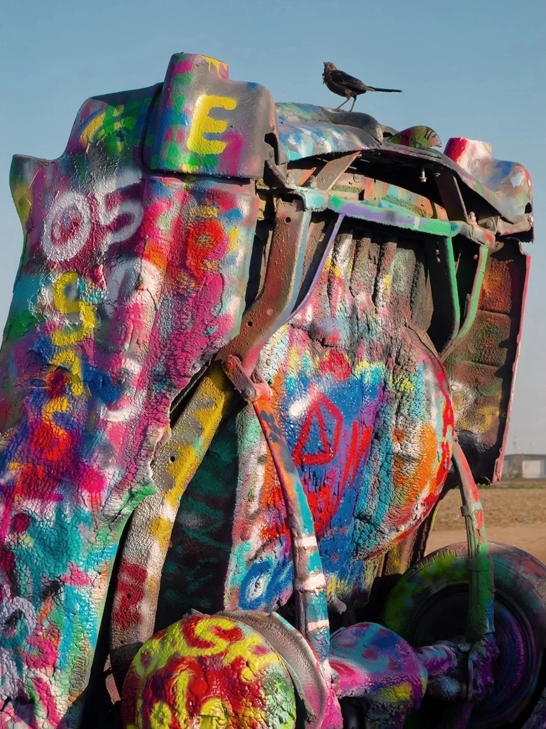 Colorfully painted, rusty vintage motorcycle with a bird perched on top against a clear sky.