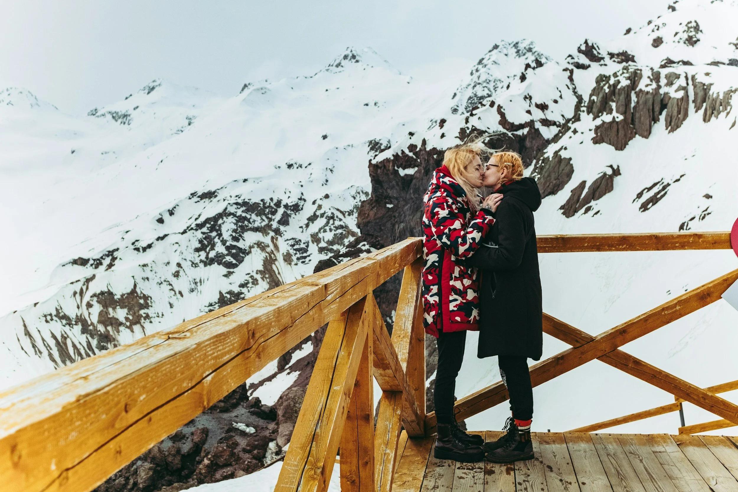 A couple kisses on a patio in snowy mountains