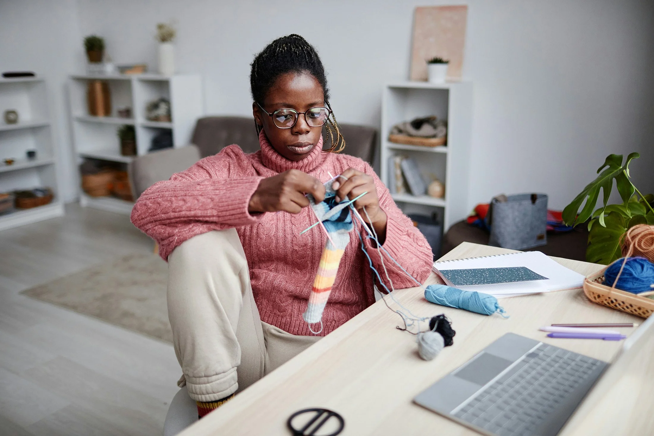 A person in a pink sweater sits at a desk and knits