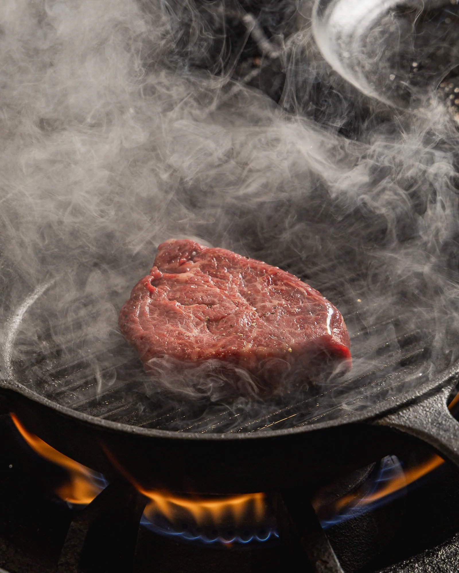 photo of eye fillet wagyu meat griling in a pan with a lot of smoke