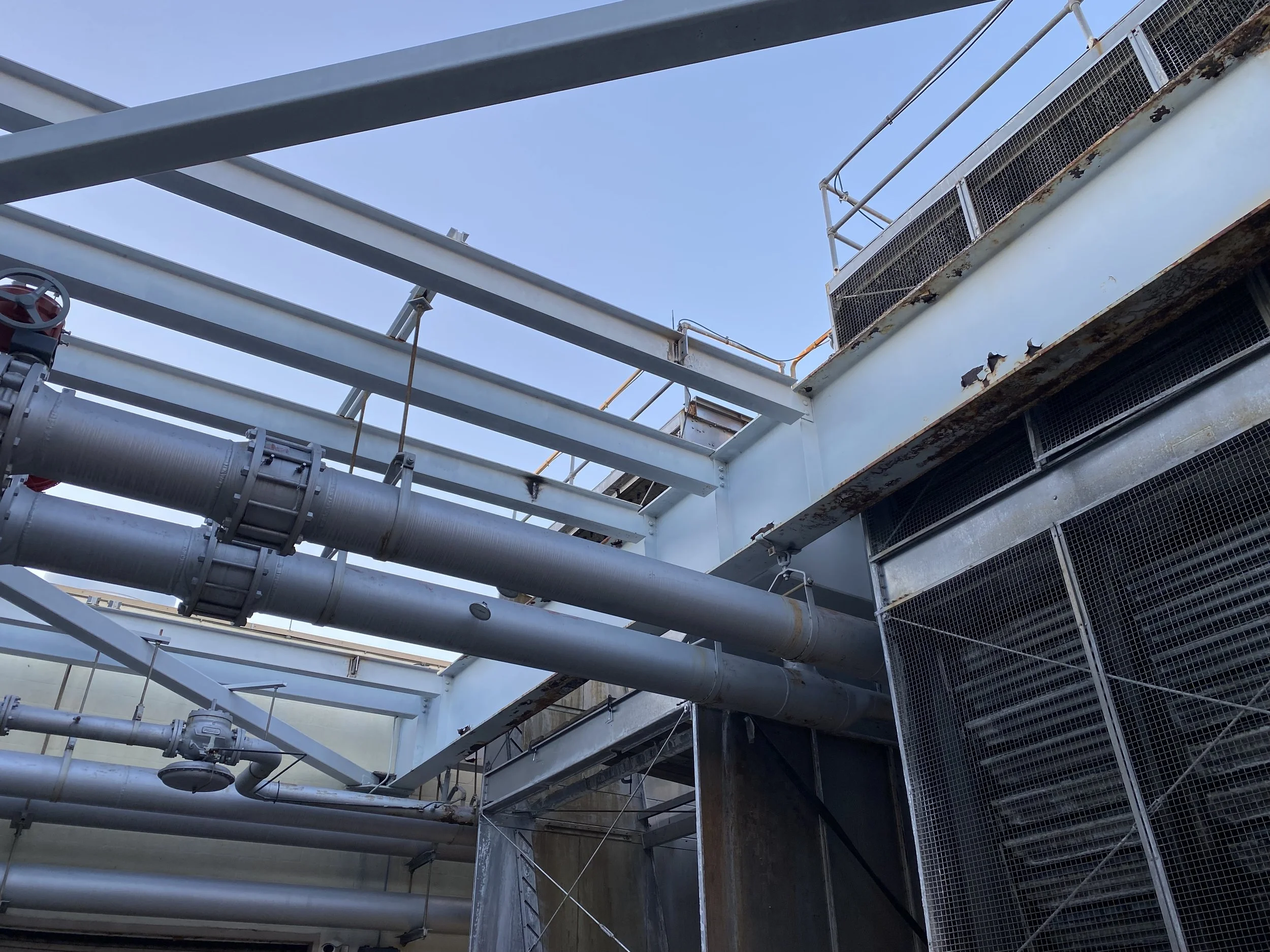 View of an industrial structure with metal pipes, vents, and a metal platform, under a clear blue sky.