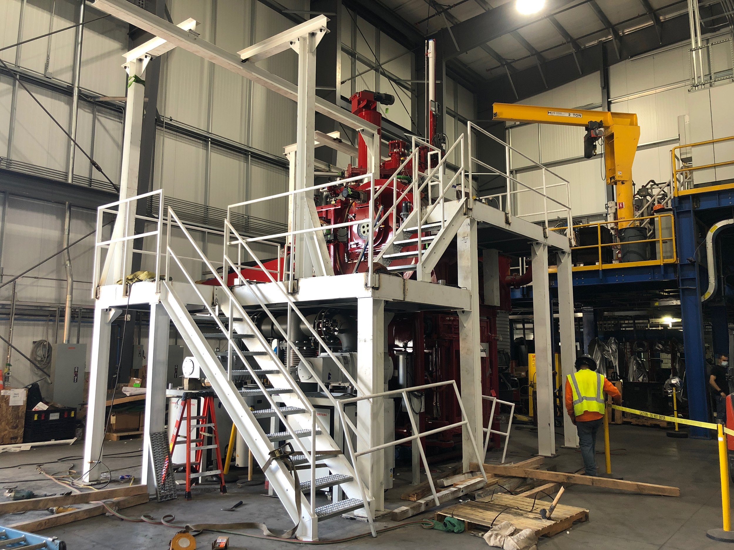 Industrial warehouse with construction scaffolding, equipment, and workers in safety vests.