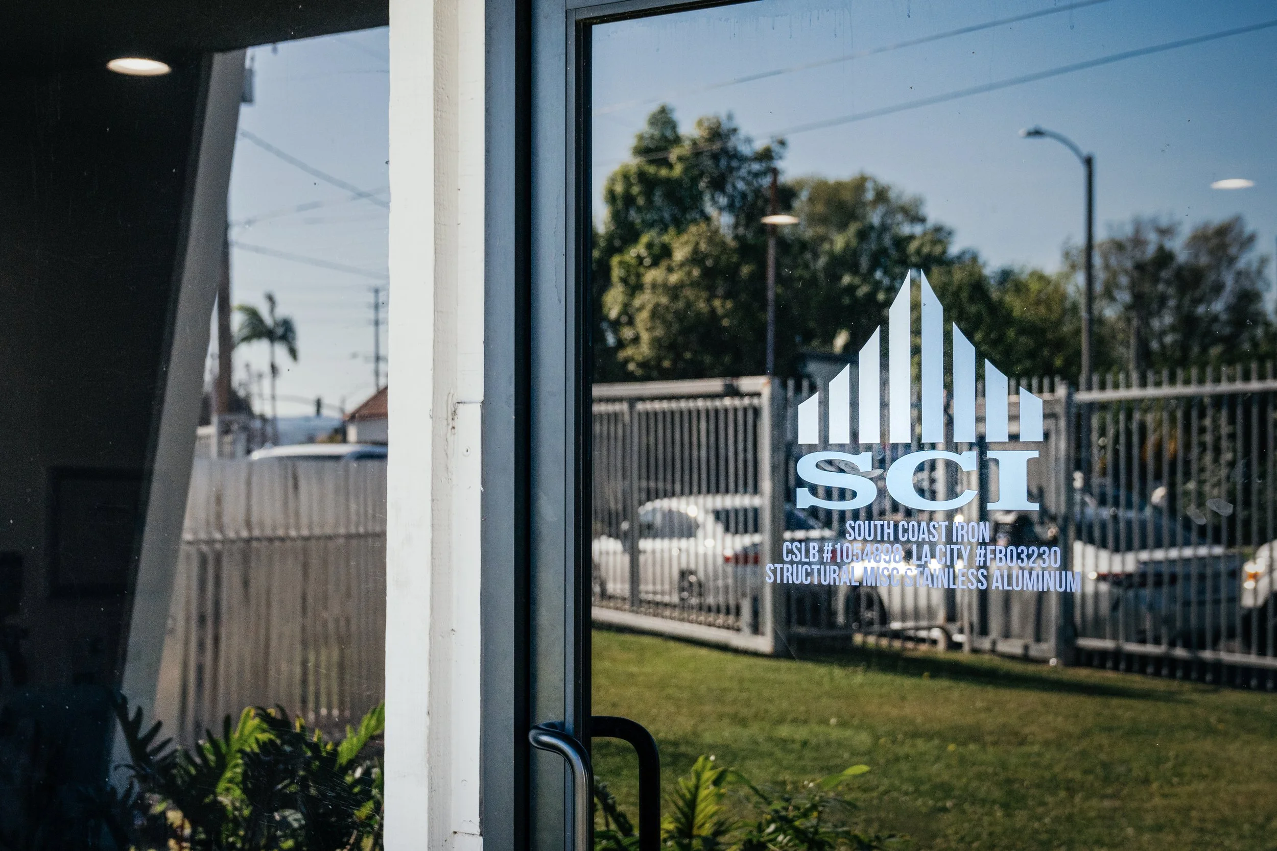 Glass door with logo and text, reflecting outdoor scene of trees, fence, and streetlights.