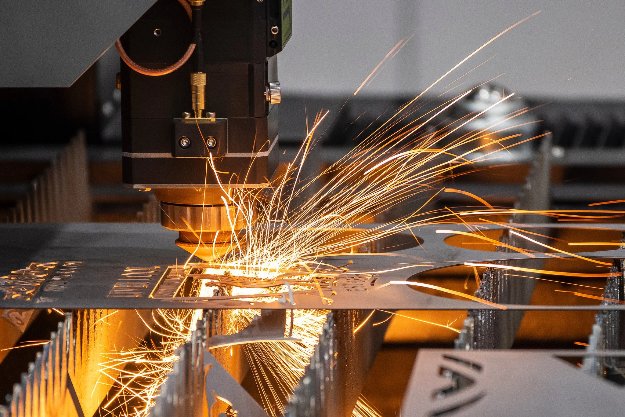 A laser cutting machine cutting through metal, producing sparks and bright light as it engraves or cuts intricate patterns.