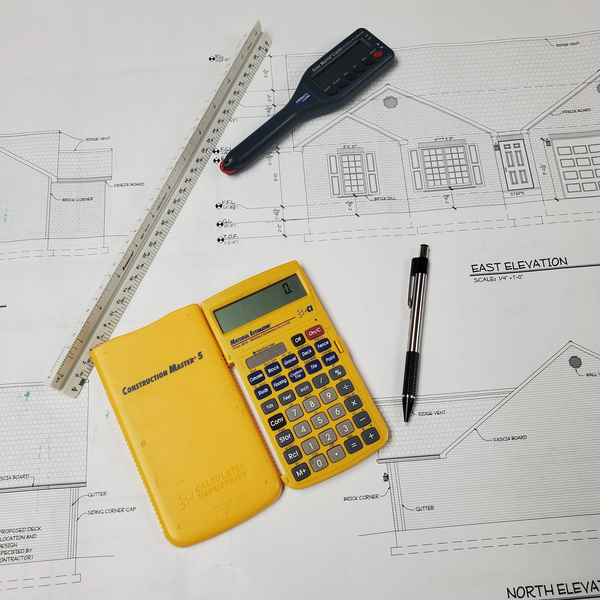 Architectural blueprint of a house with a yellow construction calculator, a black pen, a digital calculator, a gray level, and a white ruler placed on top of the blueprints.