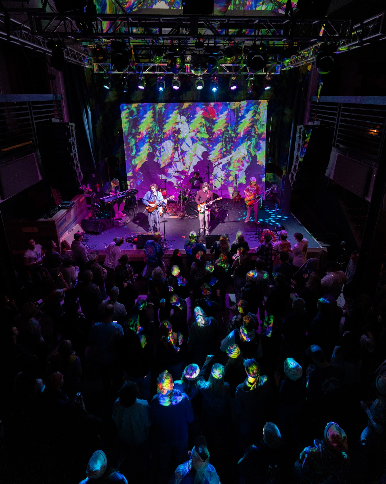 A live music concert with a band performing on stage, colorful lighting, and a crowd of people enjoying the show.