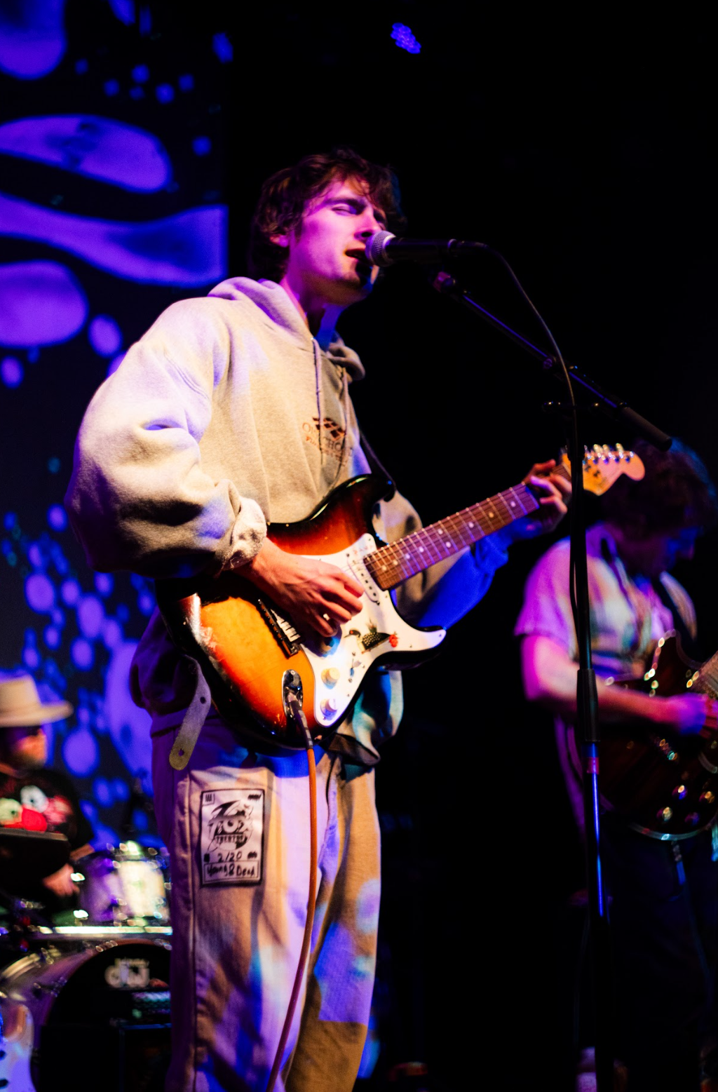 Young man playing an electric guitar and singing into a microphone on stage with blue and purple lighting