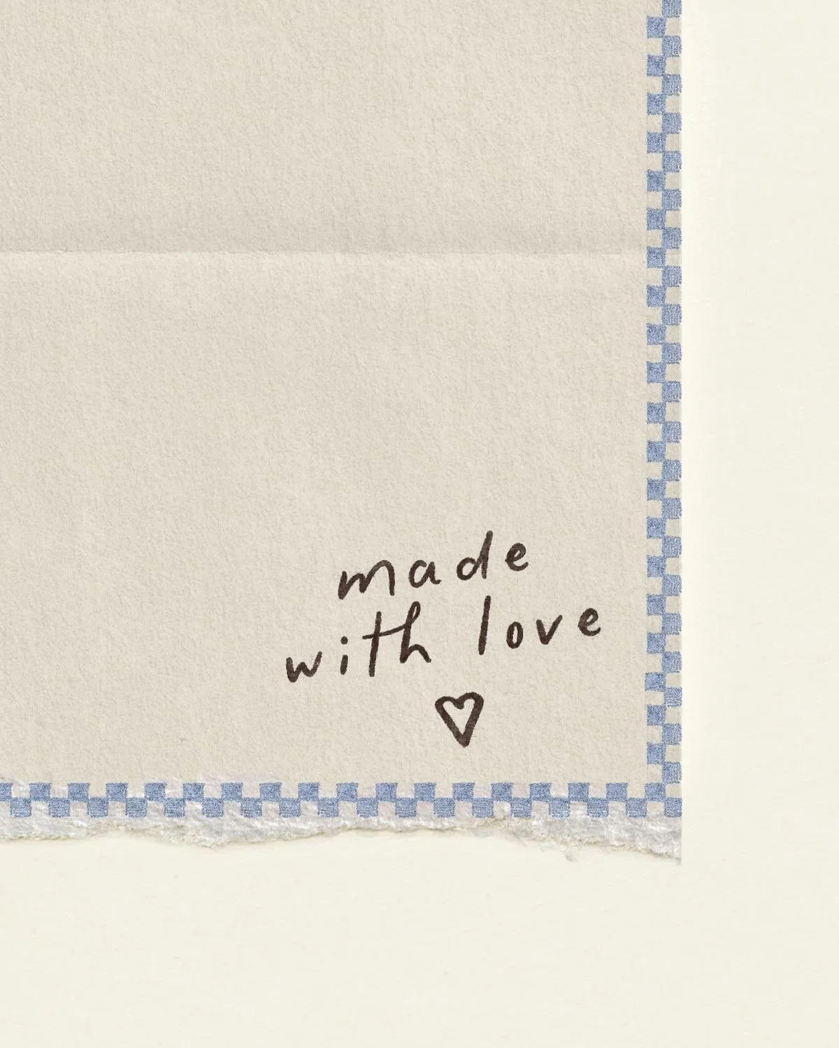 Close-up of a white fabric cloth with a blue stitched border and handwritten text that says 'made with love' with a small heart symbol underneath.