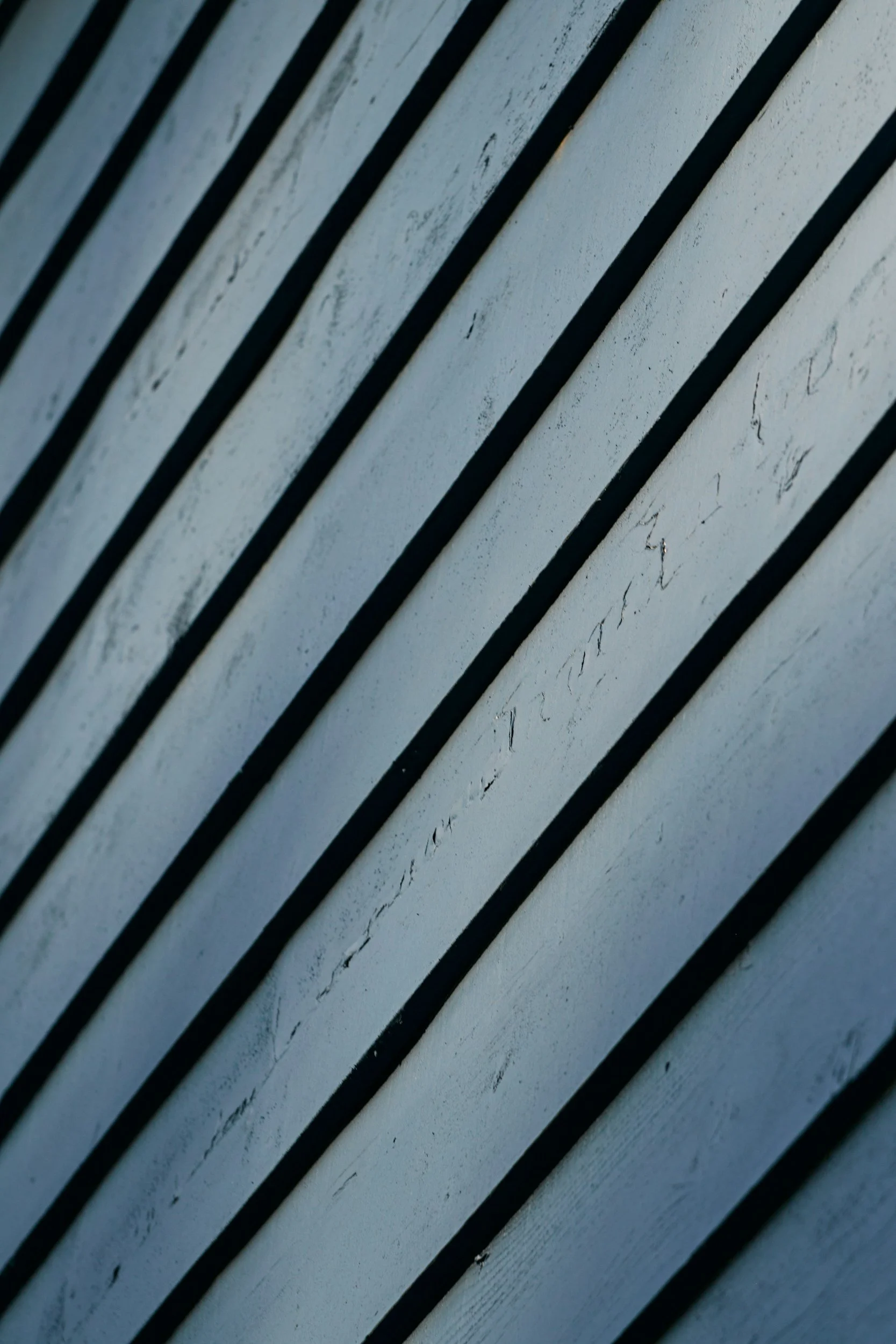Close-up of a wall with diagonal black slats and weathered white paint.