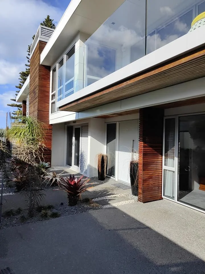 Modern residential building with large glass windows, wooden accents, and potted plants outside.