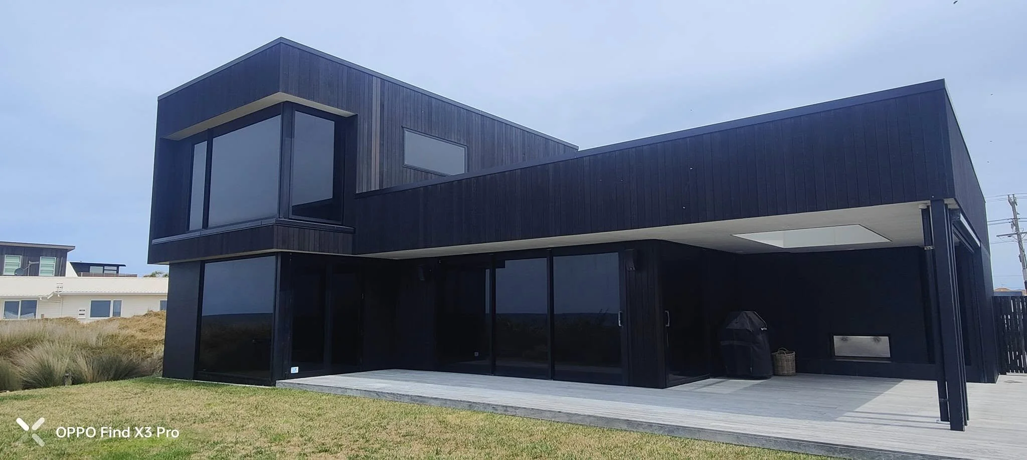 A modern two-story house with black exterior walls, large windows, and a wooden deck in the foreground.