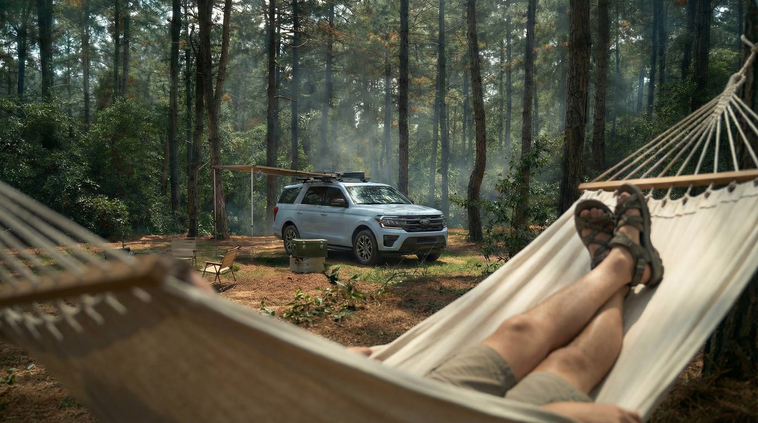 Persona descansando en una hamaca en un bosque, con una camioneta en el fondo y equipo de camping cerca.