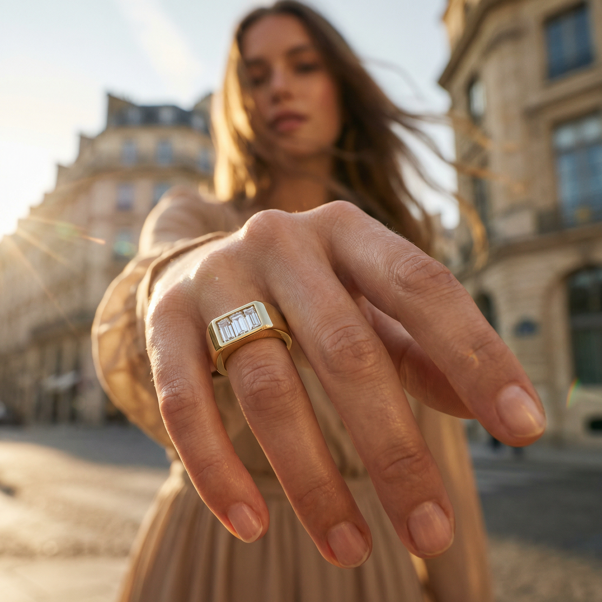 Mujer mostrando un anillo de oro con piedras preciosas en el centro, en una calle con edificios antiguos al fondo y la luz del sol al amanecer o atardecer.