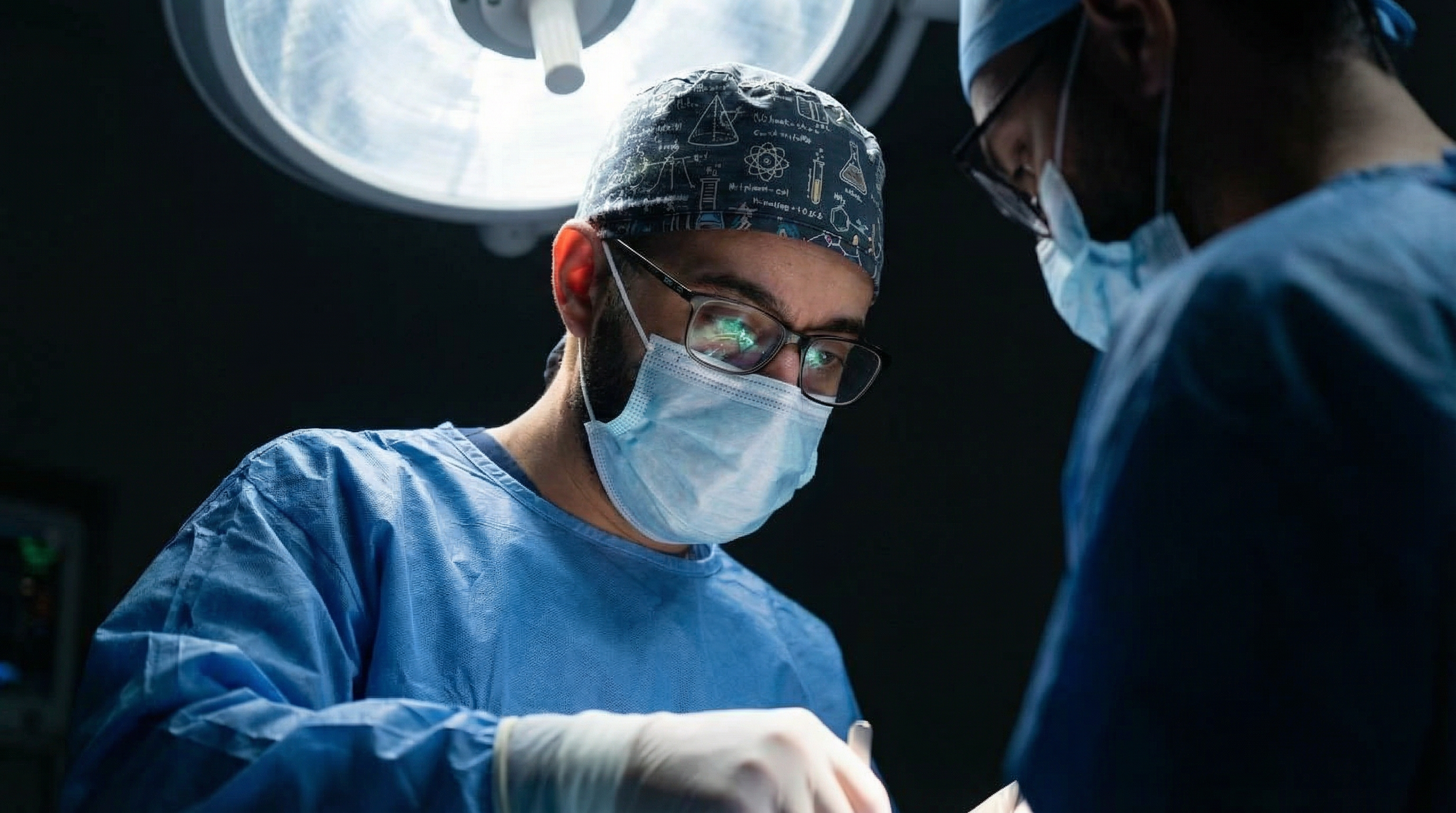 Dos cirujanos en un quirófano realizando una operación, con una lámpara quirúrgica en el techo iluminando la escena.