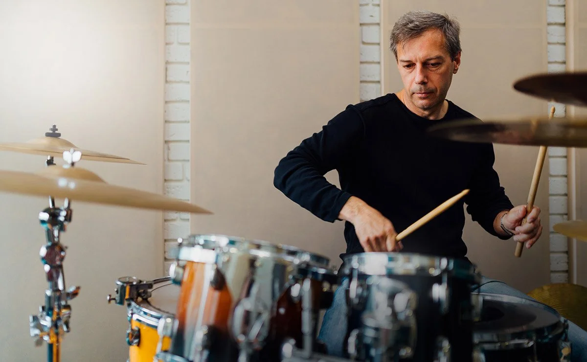 A man playing drums in a room with beige walls and white brick accents.