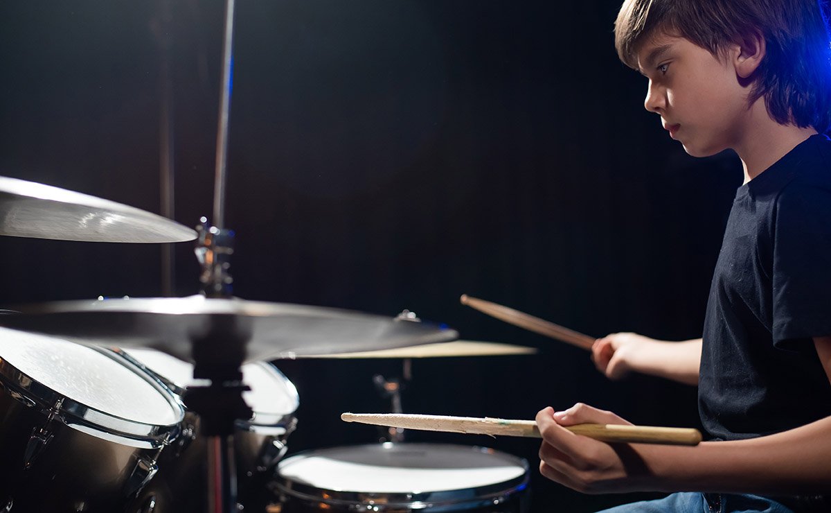 A young boy playing the drums in a dimly lit room.