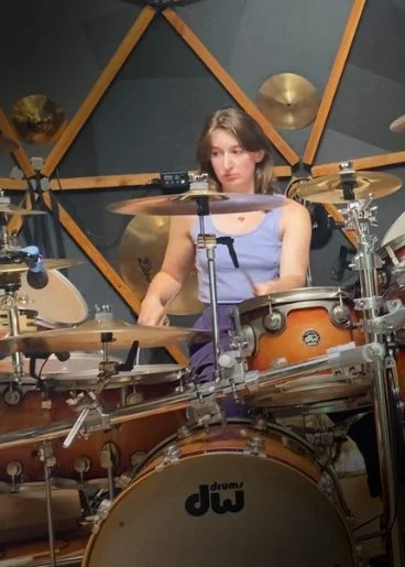 A young woman playing a drum set in a music studio.