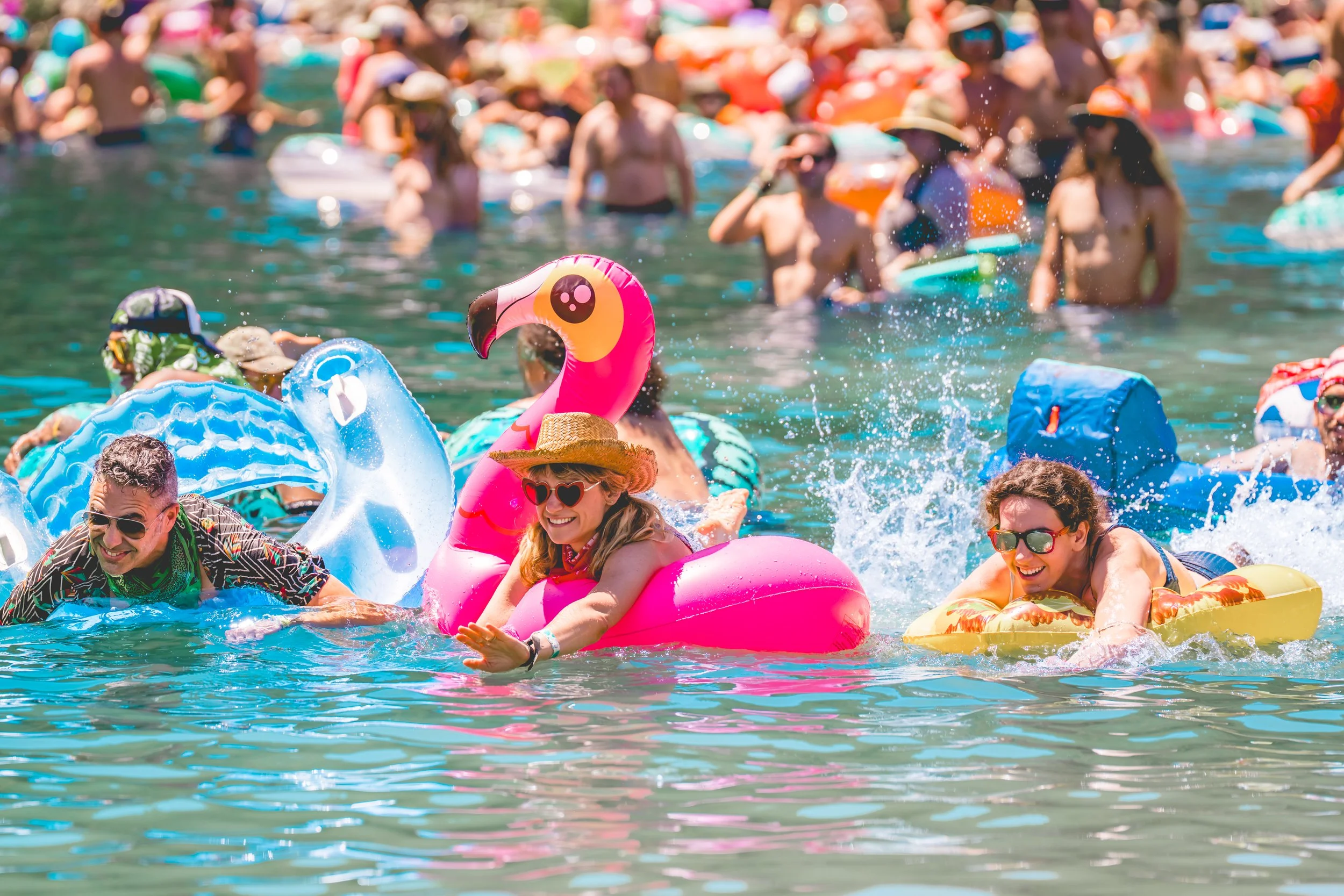 People enjoying a crowded beach with colorful inflatables, including a pink flamingo float, on a sunny day.