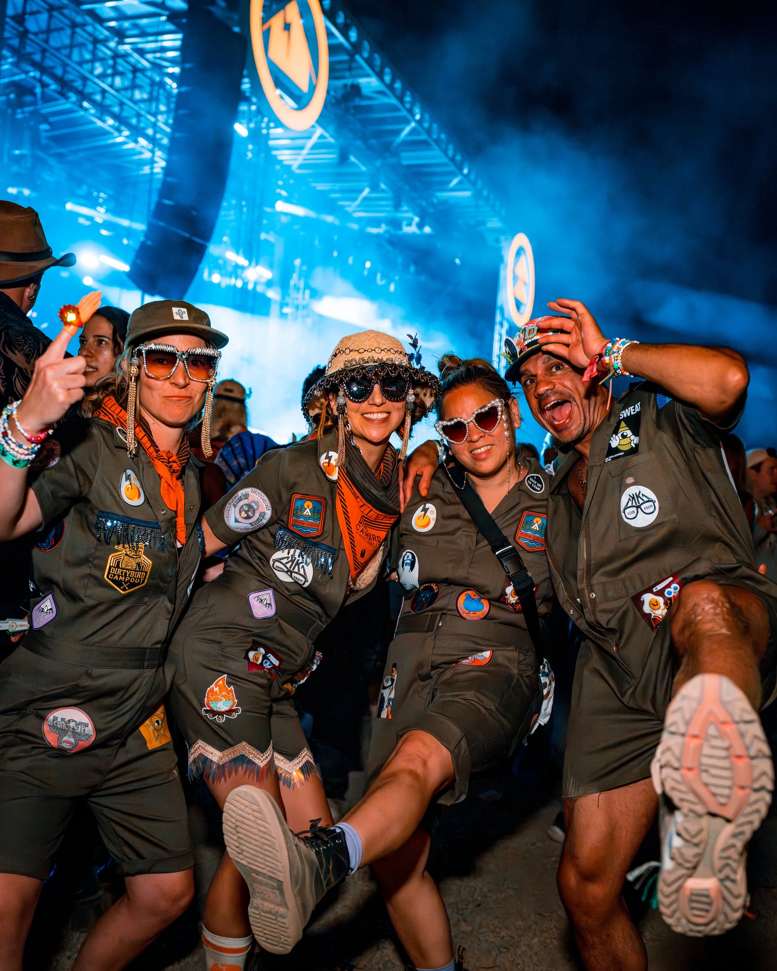 Group of people at a music festival wearing matching outfits and accessories, dancing and enjoying themselves with joyful expressions.