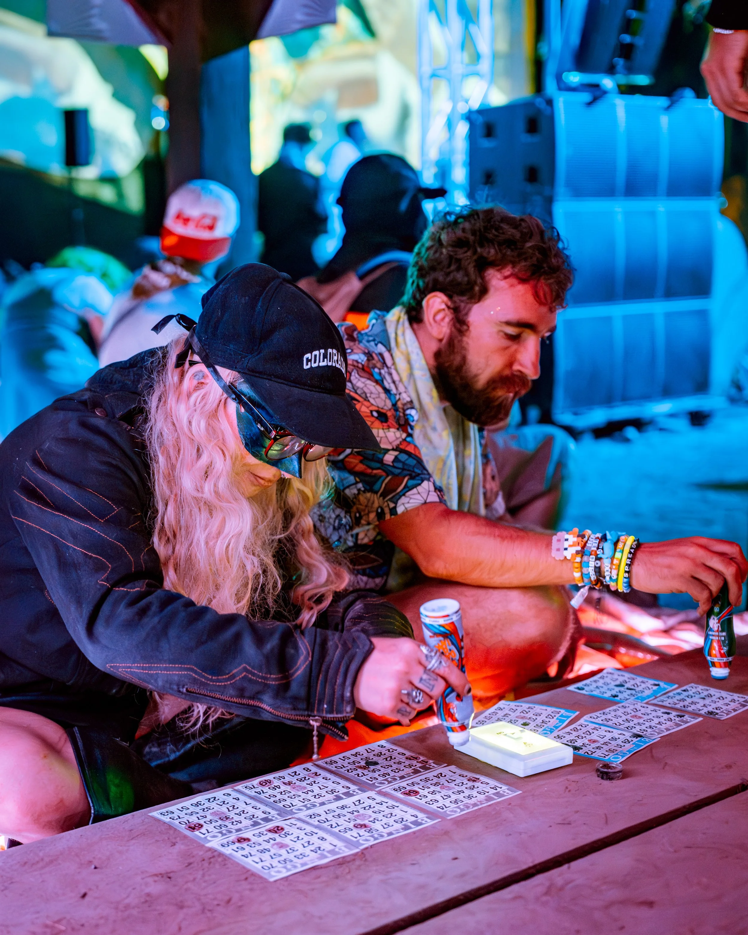 People playing bingo at an outdoor event with colorful lighting and tents.