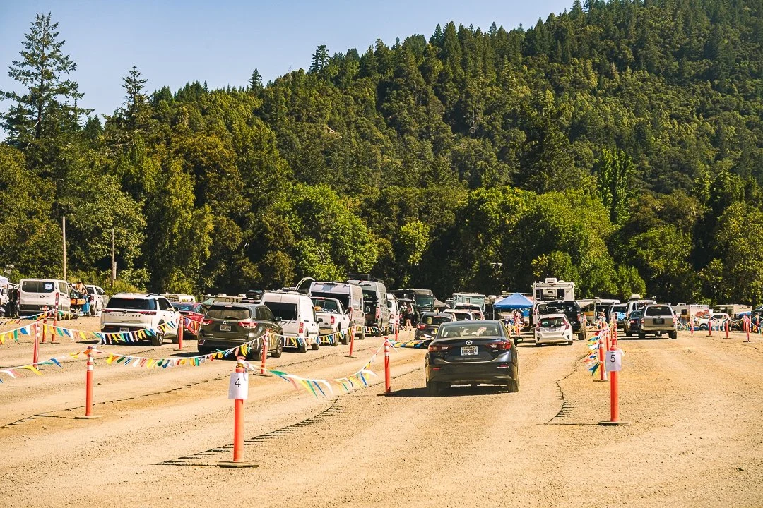 On-Site Thursday Vehicle: cars and campers lined up on a dirt road for Thursday arrival, with wooded hills behind, at Northern Nights.