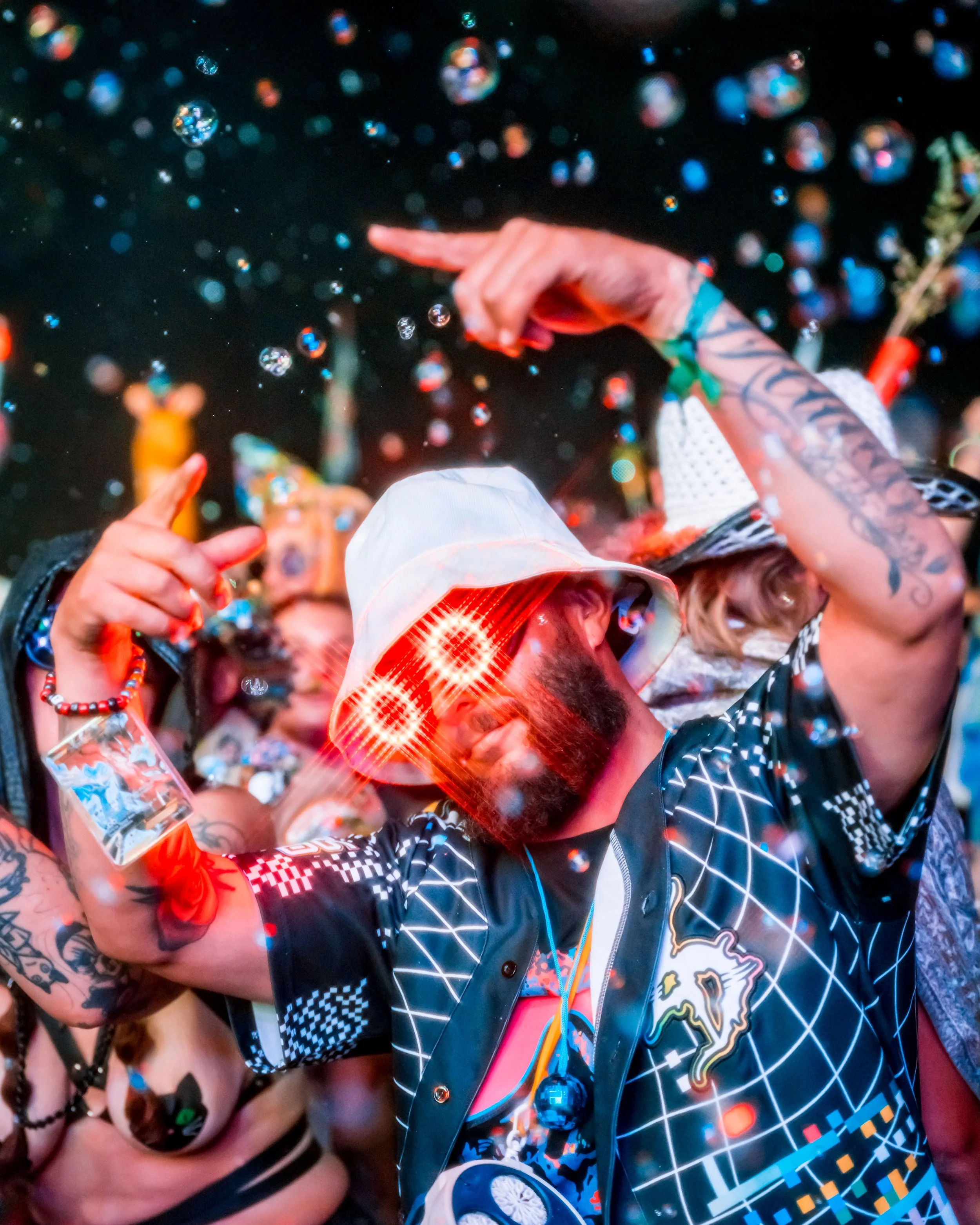 Person dancing at a party with colorful lights and bubbles, wearing a white bucket hat and glasses with red glowing effects.