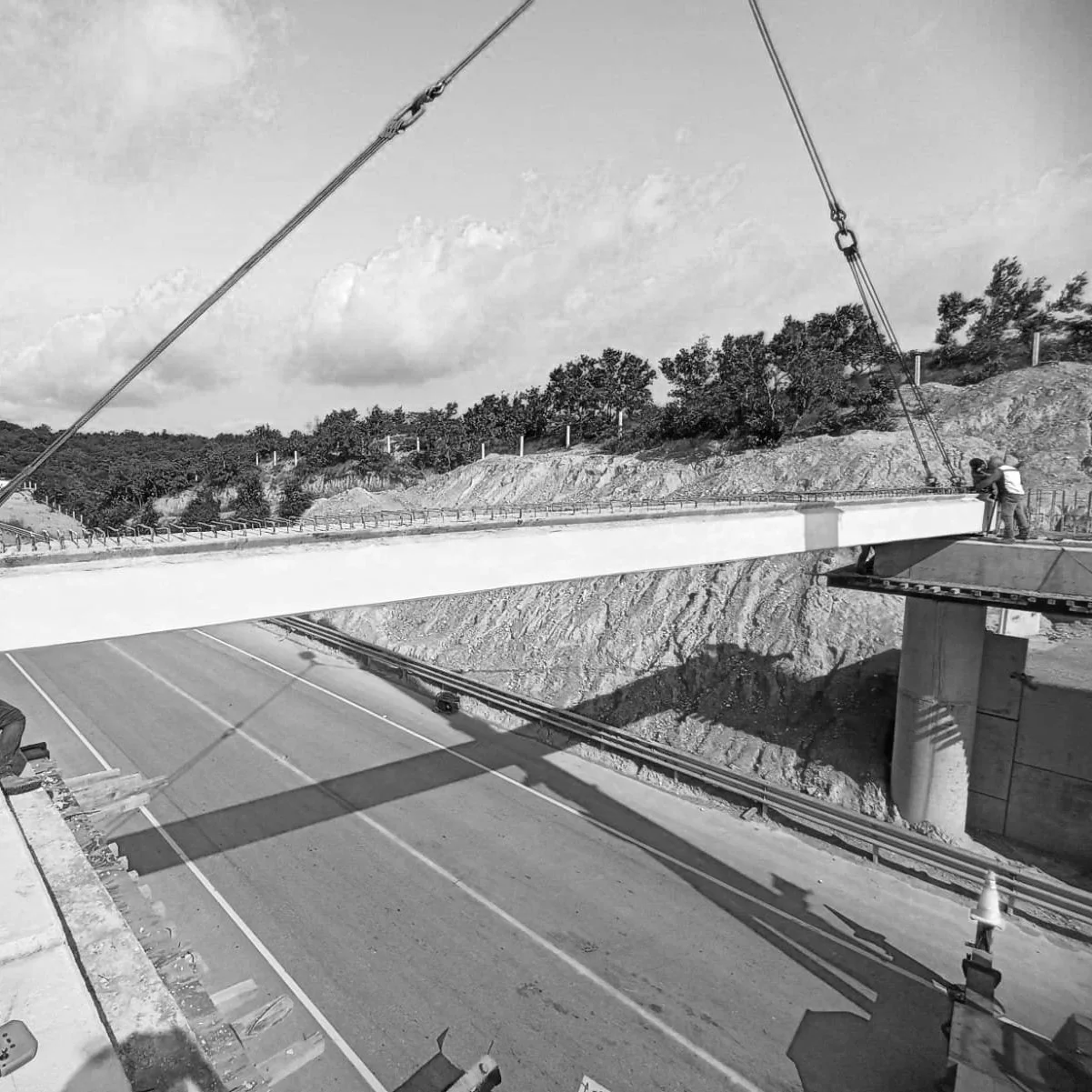 Construcción de un puente en una carretera, con trabajadores y maquinaria en un entorno rural.