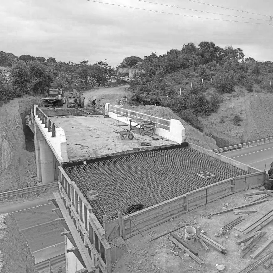 Construcción de un puente con estructura de acero y trabajo en progreso en un entorno rural.