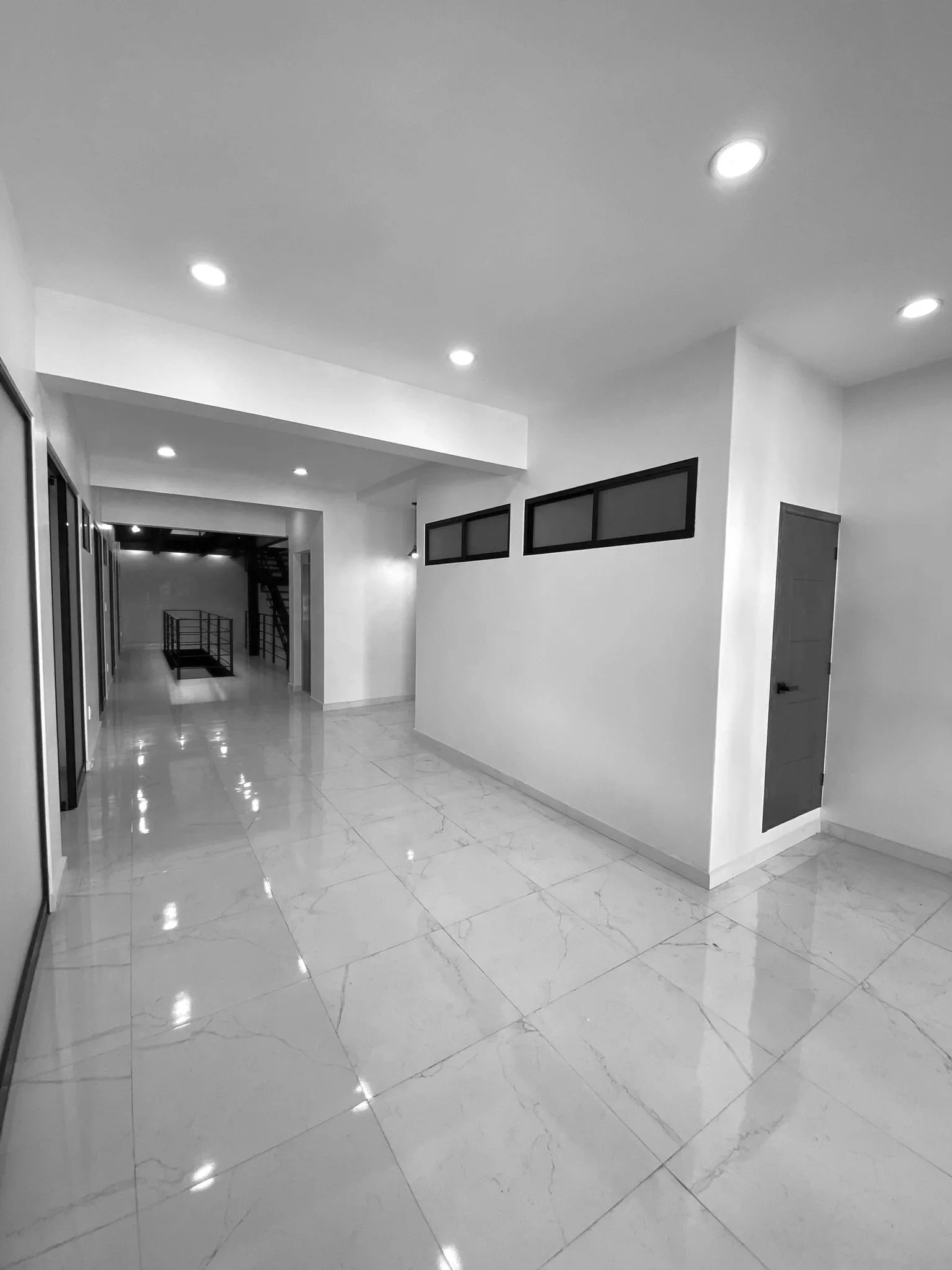 Pasillo interior de piso con suelo de mármol, paredes blancas y ventanas de cristal en la parte superior. Iluminación empotrada en el techo. Estado moderno y limpio.