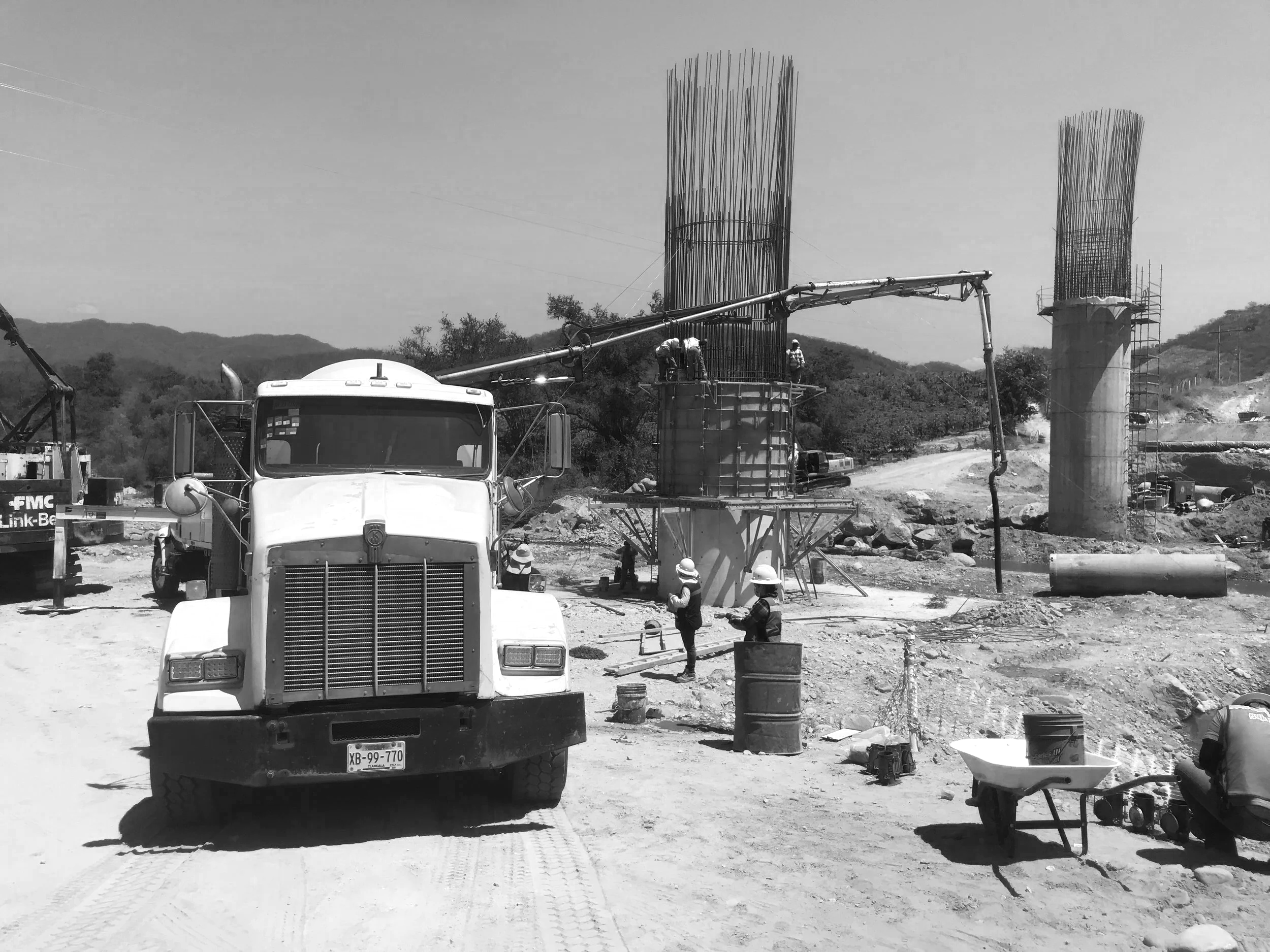 Obra en construcción con columnas de concreto en proceso y maquinaria en un ambiente rural