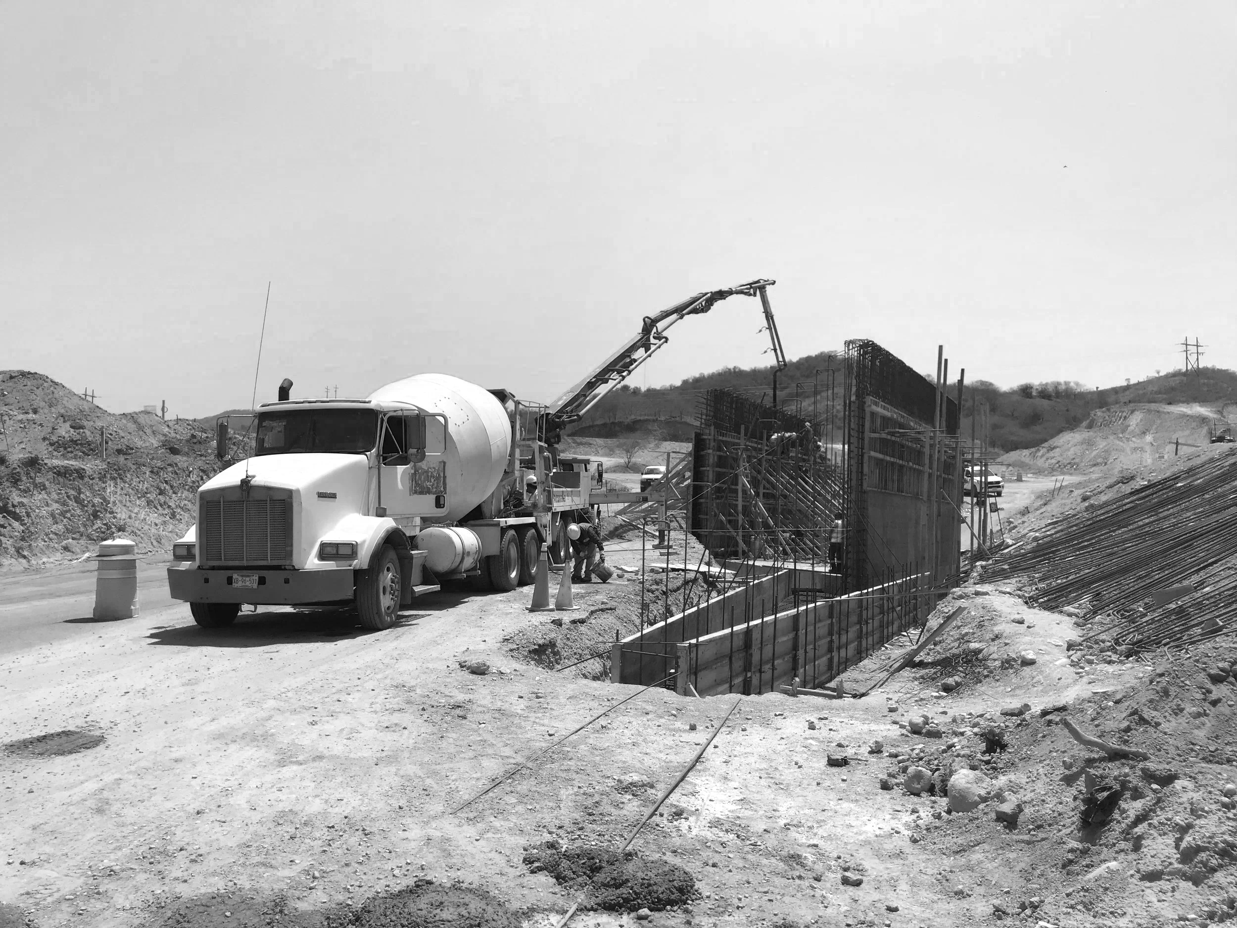 Camión mezclador y maquinaria en un sitio de construcción para una estructura de cimentación con barras de acero y encofrados en proceso.
