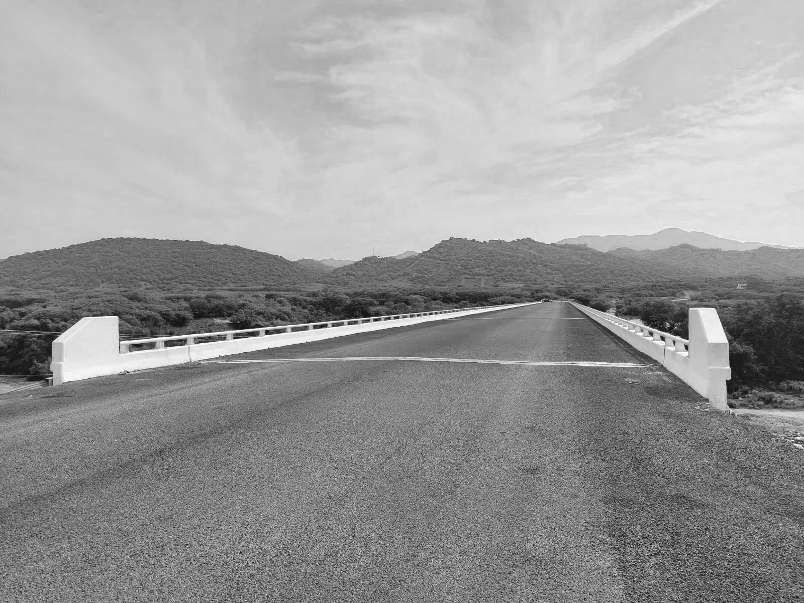 Puente de carretera en un paisaje montañoso con cielo nublado en escala de grises.