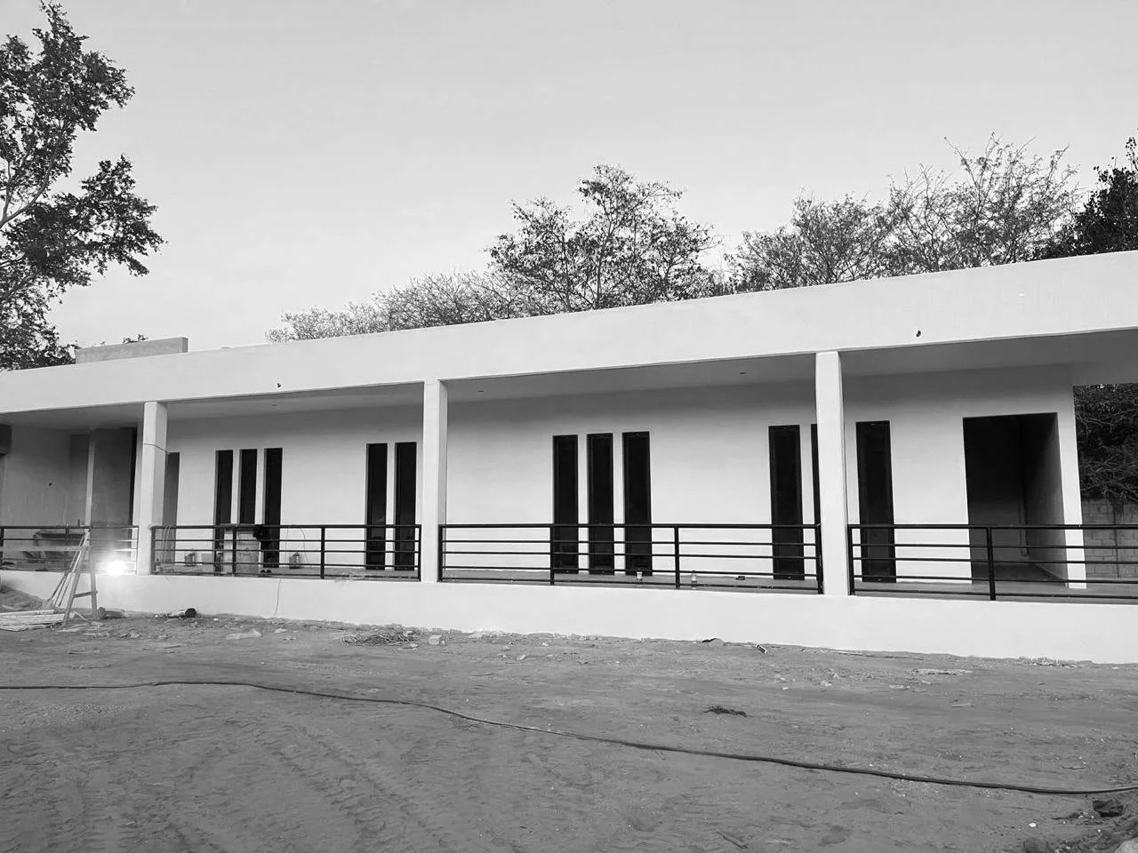 Edificio moderno en construcción en un entorno al aire libre, con paredes blancas y ventanas altas, y un barandal negro en el balcón.