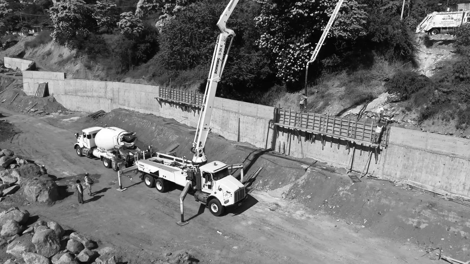 Construcción de una pared o muro de concreto con maquinaria y obreros en un terreno de tierra.