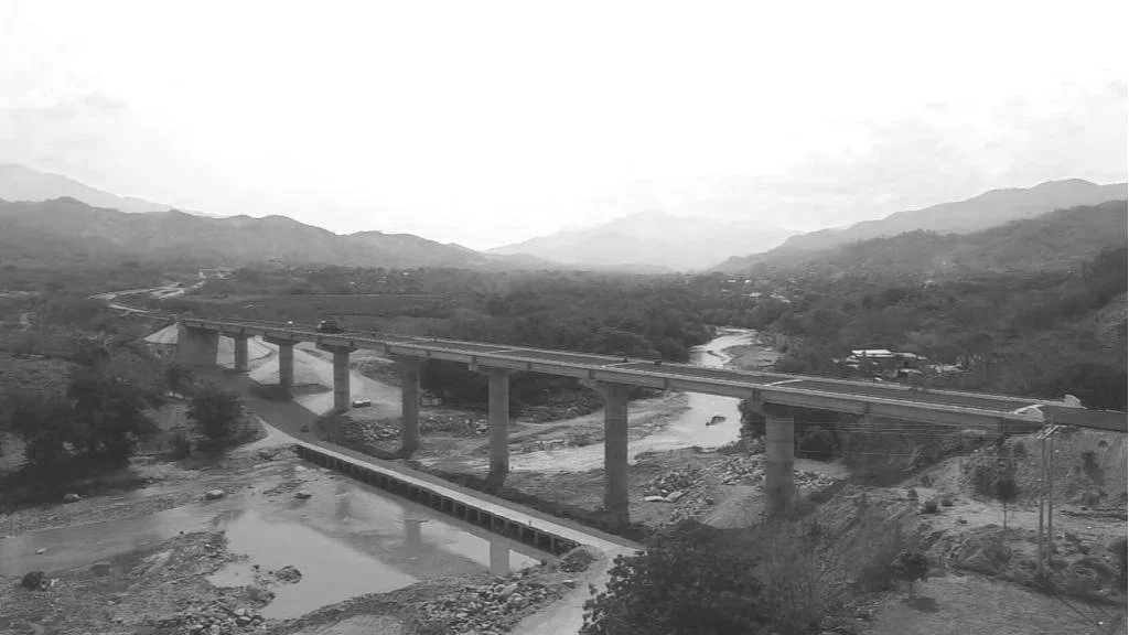Vista en blanco y negro de un puente sobre un río en un paisaje montañoso.