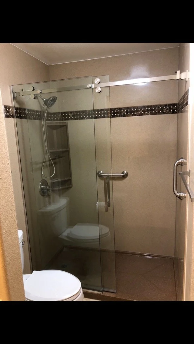 Frameless glass walk-in shower installation with sliding barn-style door hardware and built-in wall niche shelving