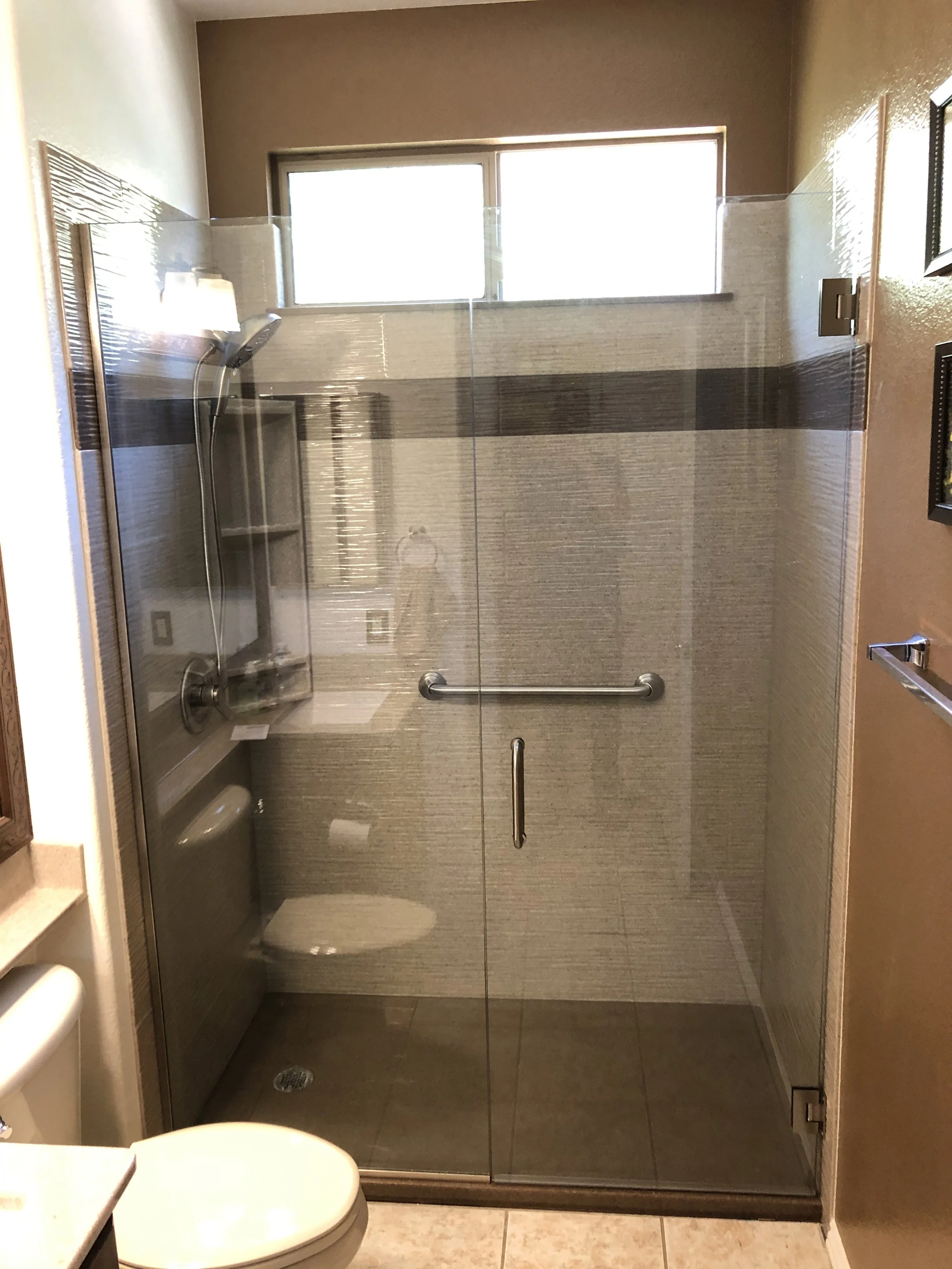 Custom glass walk-in shower with frameless door, grab bar installation, and modern wall surround system