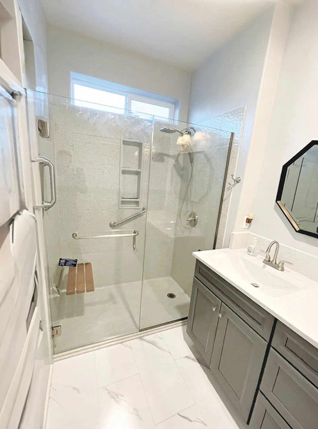 Frameless glass walk-in shower with vertical mosaic tile accent wall and granite vanity countertop in a contemporary bathroom renovation.