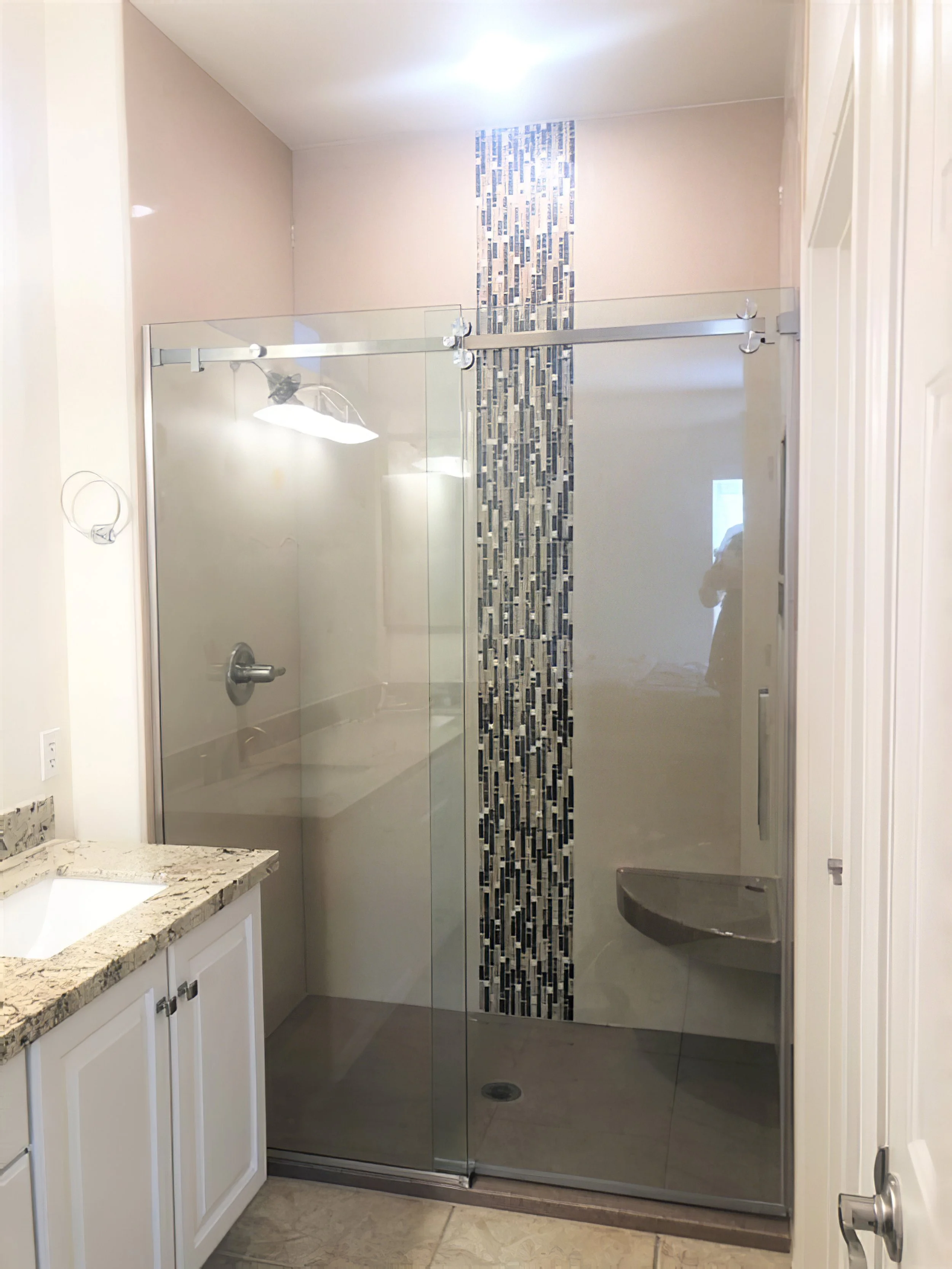 Frameless glass shower enclosure with sliding door, vertical mosaic tile feature wall, and built-in corner bench.