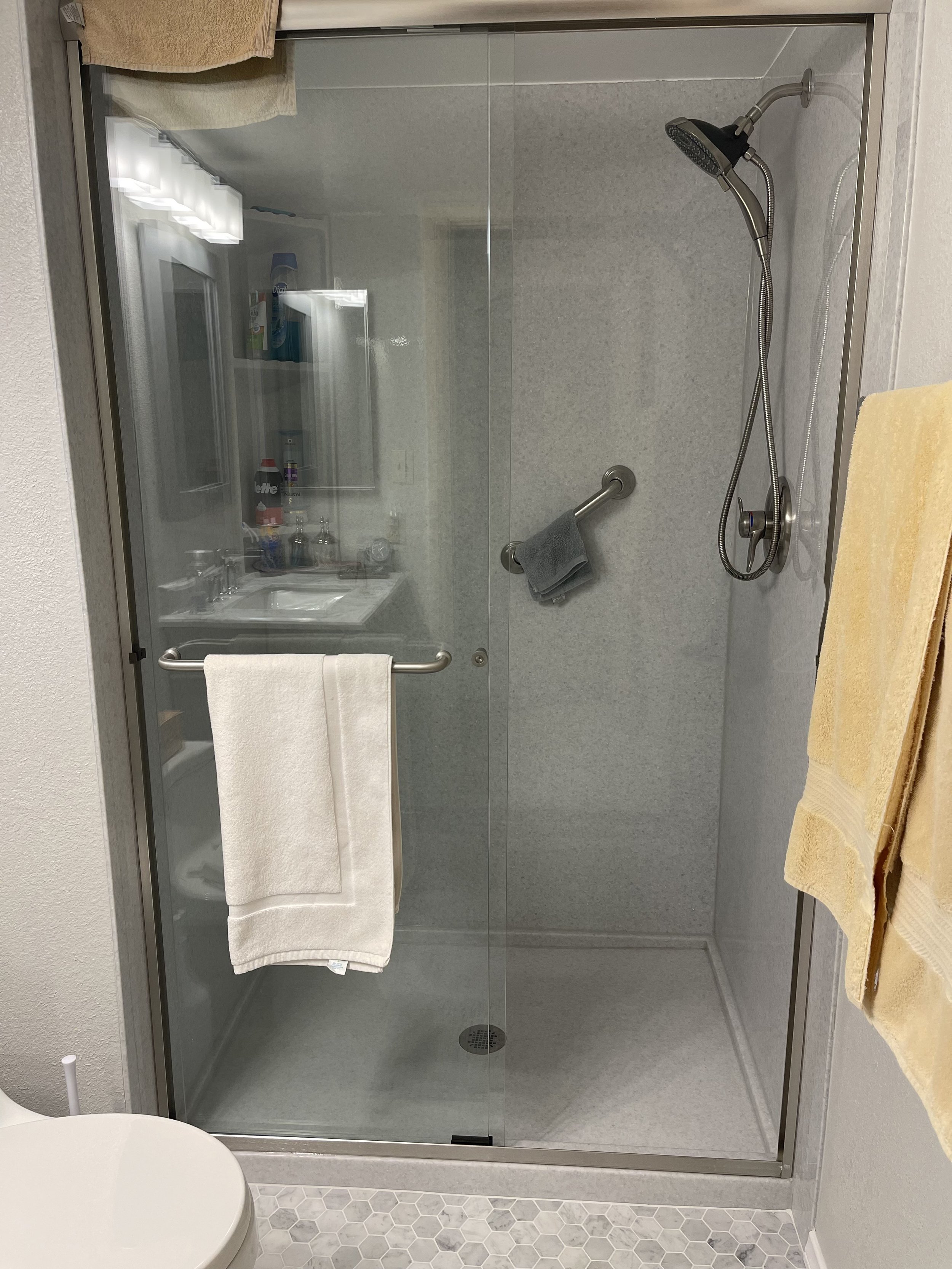 Frameless sliding glass shower doors with mosaic tile accent band and built-in wall shelving in tub to shower conversion