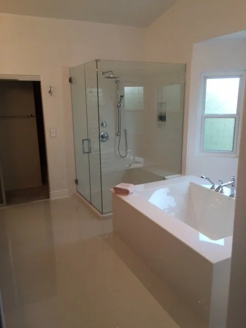 Frameless corner glass shower with chrome fixtures, built-in bench, and decorative tile accent border.
