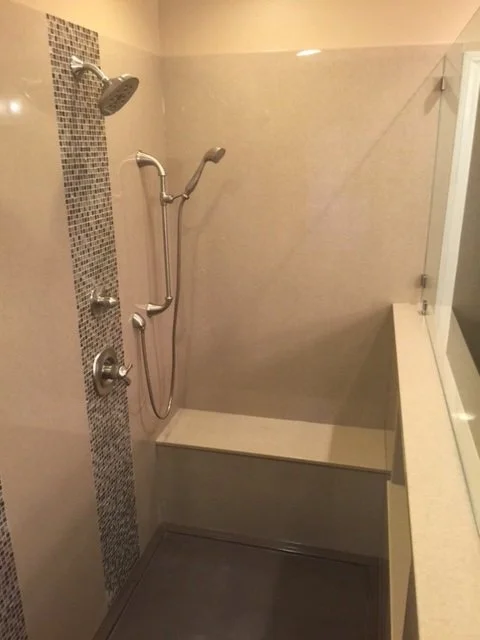 Walk-in shower remodel with built-in bench seating, handheld shower head, and vertical mosaic tile accent strip in neutral stone surround.
