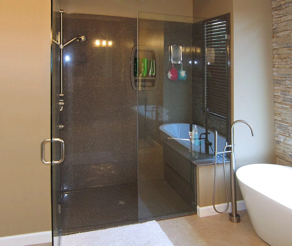 Frameless glass shower enclosure with dark tile surround and soaking tub