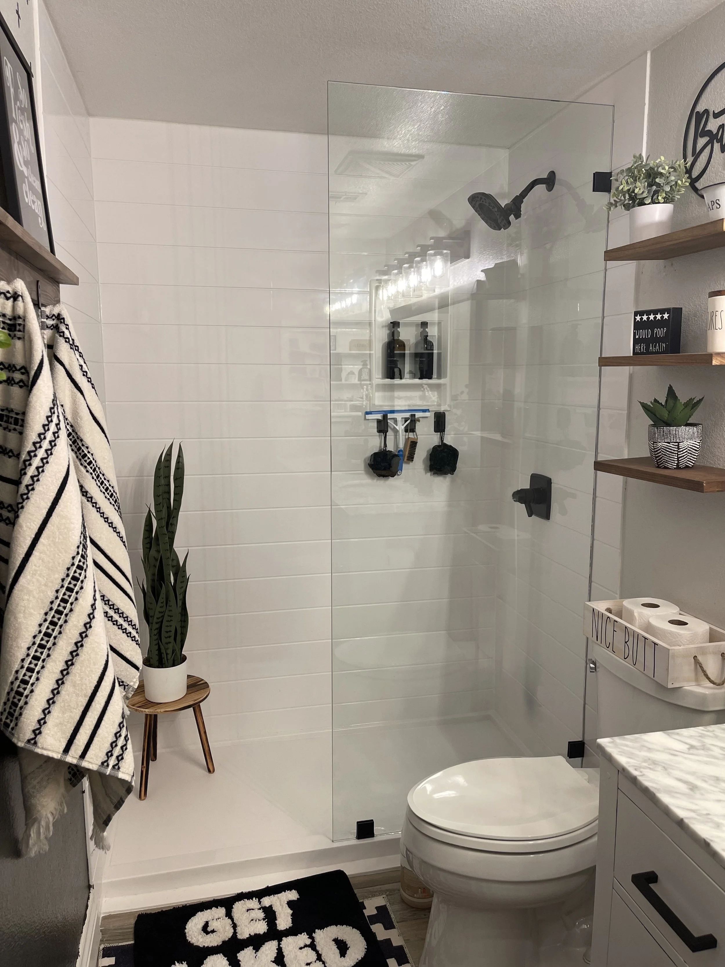 Custom walk-in shower with textured tile walls, half-height privacy wall, frameless glass enclosure, and handheld shower fixture